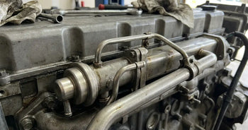 EGR cooler, valve and coolant tubing running along the valve cover of a 6.7-litre Cummins inline-six, with a wrench and shop rag resting on top