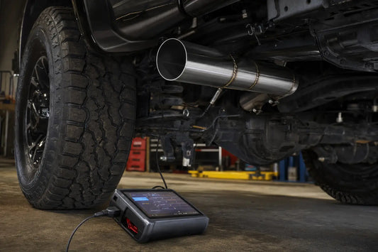 DPF delete pipe installed on a diesel truck alongside an OBD-II delete tuner connected to the diagnostic port