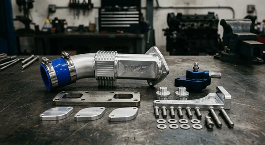 BMW M57 EGR delete kit components including billet aluminum race pipe, stainless steel block-off plate, and coolant plugs on a workshop bench
