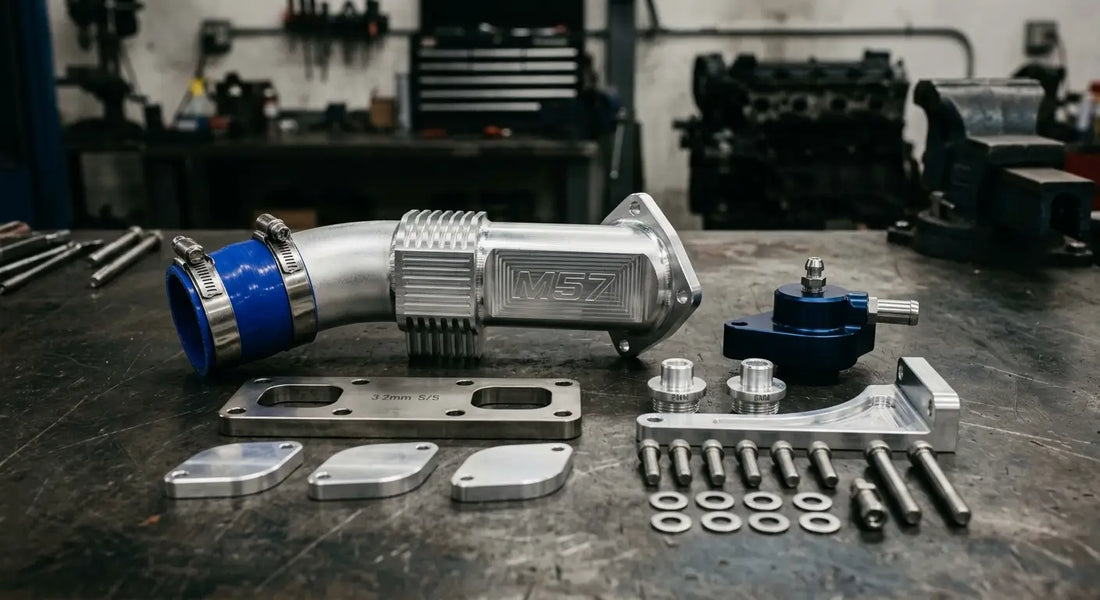 BMW M57 EGR delete kit components including billet aluminum race pipe, stainless steel block-off plate, and coolant plugs on a workshop bench