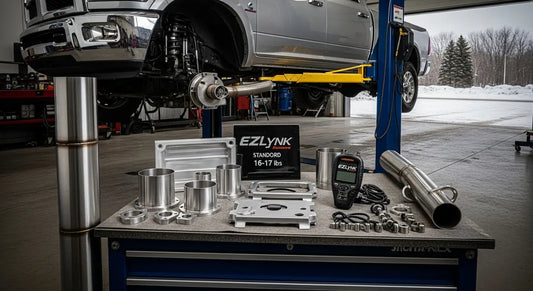 Billet aluminum EGR delete kit and 5-inch stainless DPF delete pipe laid out for installation on a 6.7L Cummins Ram 2500, with EZLynk Auto Agent 3 tuner on workbench — full delete bundle components for Canadian diesel truck build